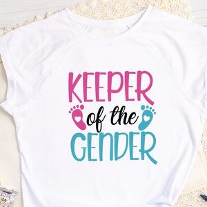 May include: White t-shirt with the text "KEEPER of the GENDER" in pink and blue lettering. The text is accompanied by a pink and blue footprint with a heart.
