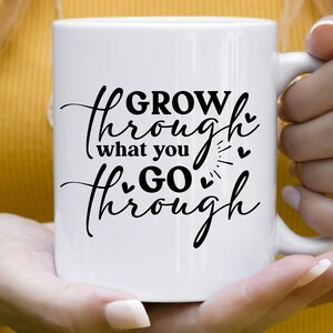 May include: White ceramic mug with black text that reads "GROW through what you GO through" with small hearts and a sunburst design.