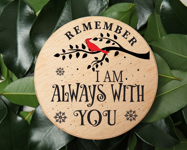 May include: A round wooden sign with the text "Remember I am always with you" in black lettering. A red cardinal bird is perched on a branch with green leaves. The sign has a snowflake design around the edges.