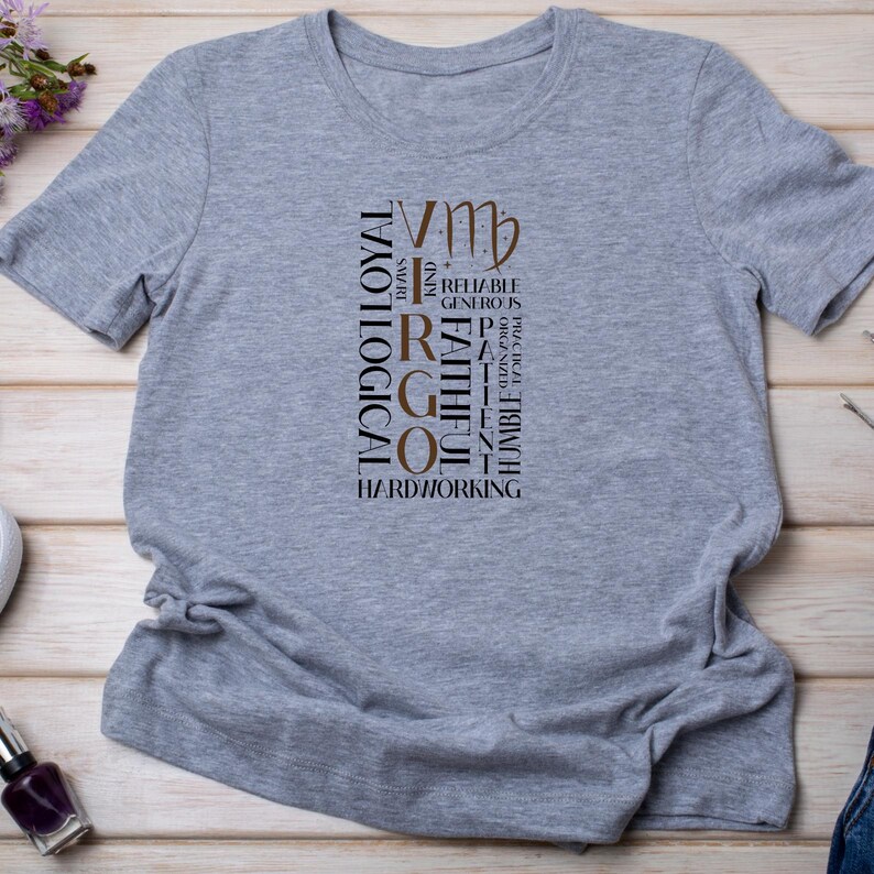 May include: A heather gray t-shirt featuring the Virgo zodiac sign. The design includes the Virgo symbol and words like "Loyal", "Logical", "Smart", "Reliable", and "Hardworking" in a vertical arrangement. The shirt is made of a soft material.