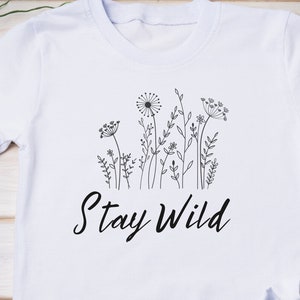May include: White t-shirt with a black line drawing of wildflowers and the text "Stay Wild".