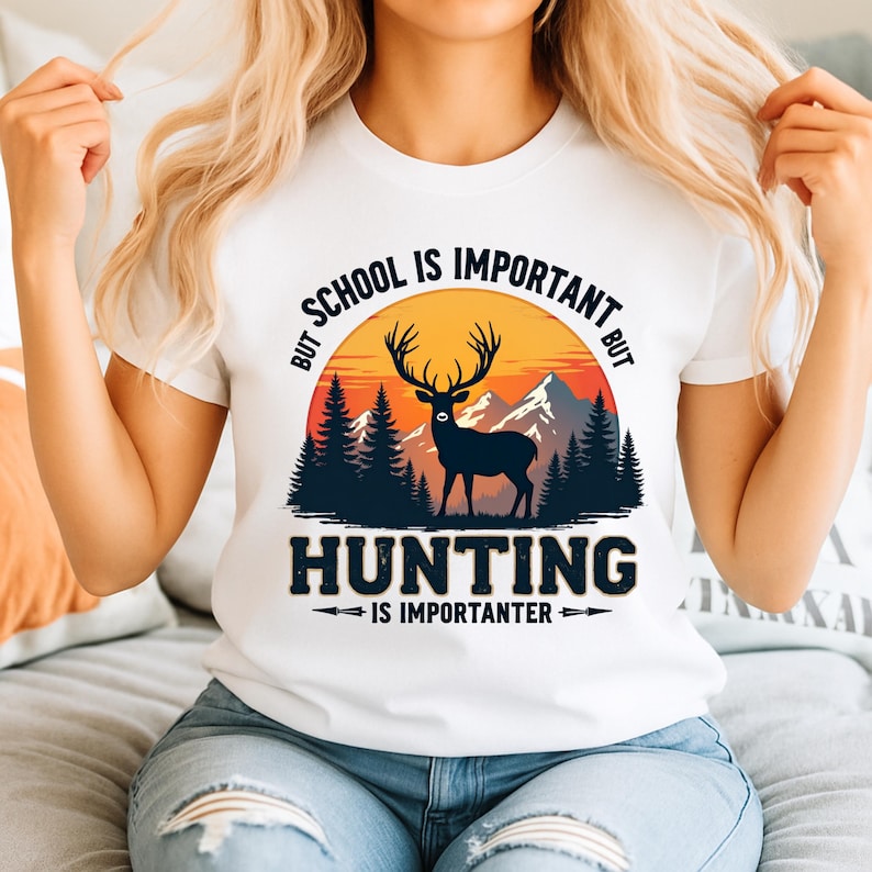 May include: White t-shirt with a graphic featuring a deer silhouette, mountains, and a sunset. The text reads "BUT SCHOOL IS IMPORTANT BUT HUNTING IS IMPORANTER". The design is in shades of black, orange, and green.