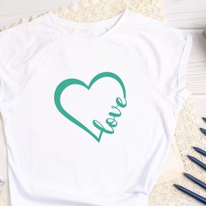 May include: White t-shirt with a teal green heart design and the word "love" written inside the heart.