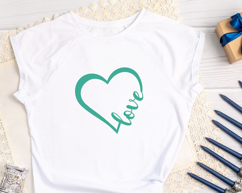 May include: White t-shirt with a teal green heart design and the word "love" written inside the heart.