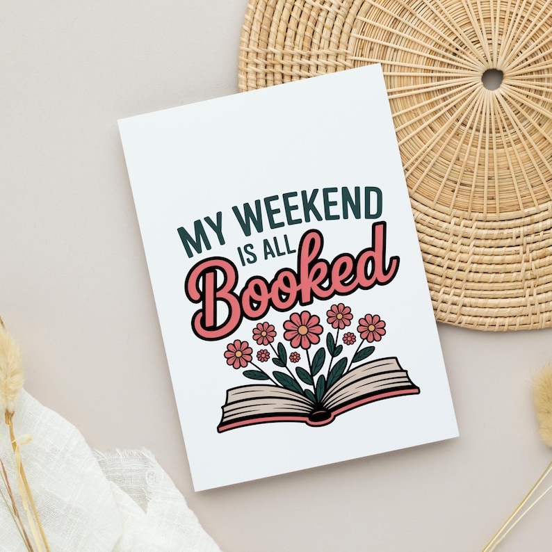 以下が含まれることがあります： 「MY WEEKEND is ALL Booked」というテキストが様々なフォントと色で書かれた白いカード。 「Booked」という単語はピンク色のレトロなフォントで書かれています。 テキストの下には、そこから花が咲いている開いた本があります。