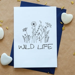 May include: A white card with a black line drawing of wildflowers and the text "WILD LIFE" printed in black.