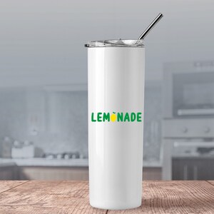 Puede incluir: Un vaso blanco de acero inoxidable con un gr&aacute;fico de "LEMONADE" verde y amarillo y una tapa plateada. El vaso est&aacute; sobre una superficie de madera.