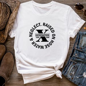 May include: White t-shirt with a black circle graphic that says "Water & Neglect. Raised on Hose" with a black "X" in the center and "Generation 1965 - 1980" written on a white rectangle.