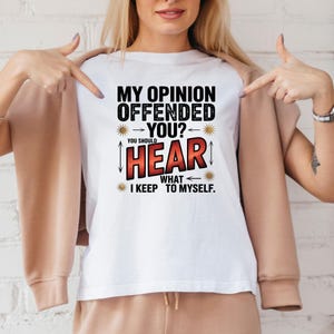 K&ouml;nnte beinhalten: Wei&szlig;es T-Shirt mit dem Text "MY OPINION OFFENDED YOU? YOU SHOULD HEAR WHAT I KEEP TO MYSELF." Der Text ist in Schwarz und Rot gehalten, mit dekorativen Elementen. Das T-Shirt wird gezeigt.