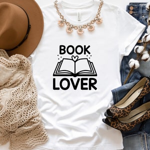 May include: White t-shirt with black text that reads "BOOK LOVER" and a graphic of an open book with a heart in the center.