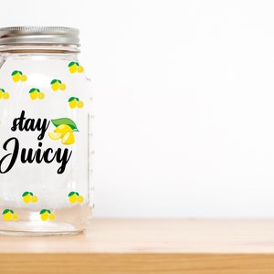 Puede incluir: Un tarro de vidrio transparente con tapa plateada y dise&ntilde;o de lim&oacute;n. El tarro tiene el texto "stay juicy" impreso.