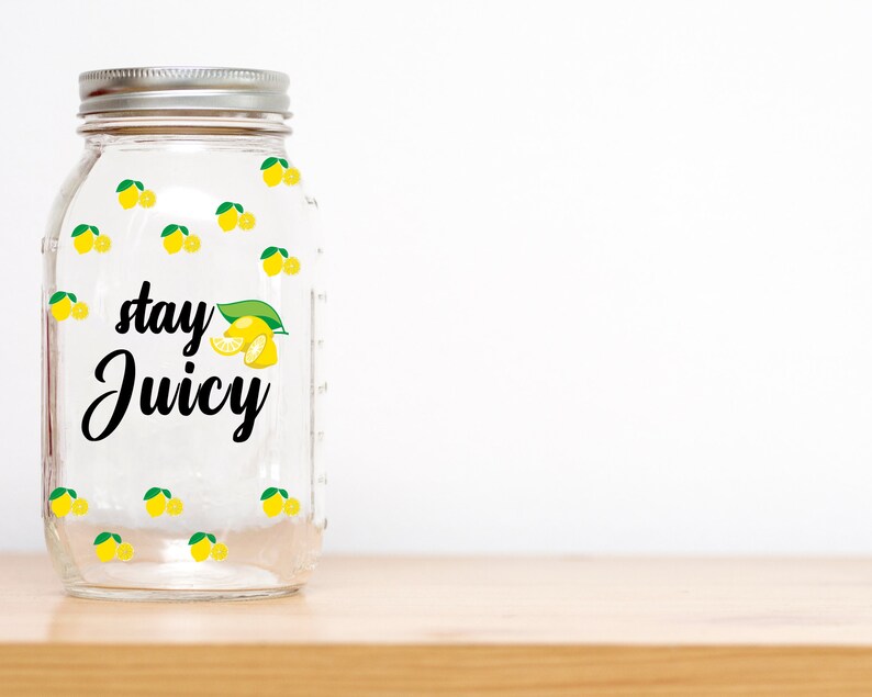 Puede incluir: Un tarro de vidrio transparente con tapa plateada y dise&ntilde;o de lim&oacute;n. El tarro tiene el texto "stay juicy" impreso.