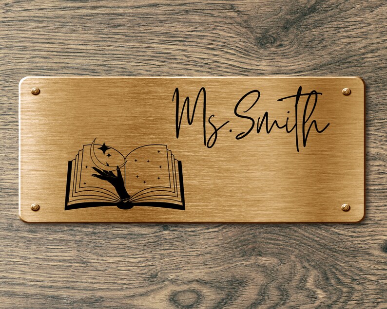 May include: A gold metal nameplate with the text "Ms. Smith" and a black and white illustration of an open book with a hand reaching for a crescent moon and stars.