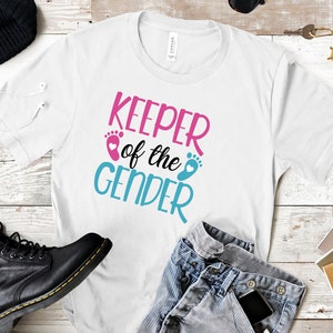 May include: White t-shirt with the text "Keeper of the Gender" in pink, blue, and white. The text is surrounded by two blue and pink footprints with hearts.