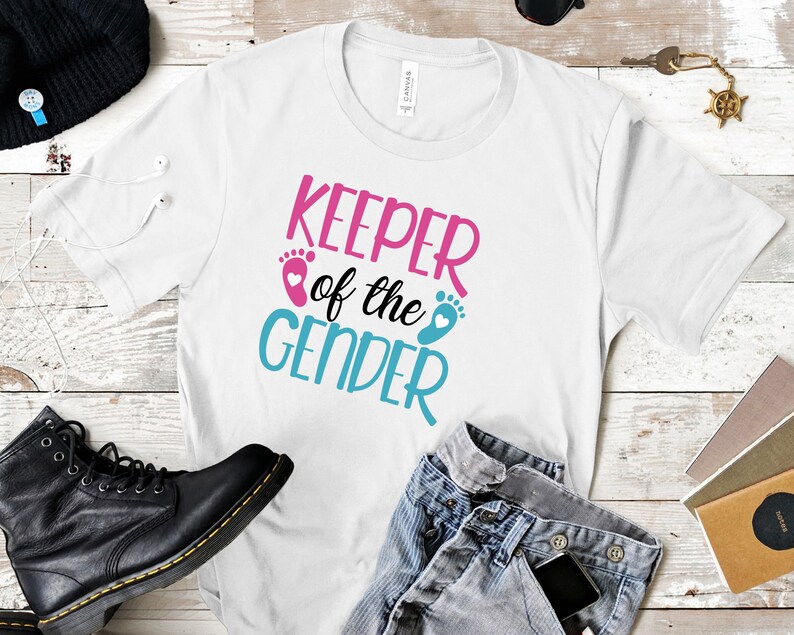 May include: White t-shirt with the text "Keeper of the Gender" in pink, blue, and white. The text is surrounded by two blue and pink footprints with hearts.