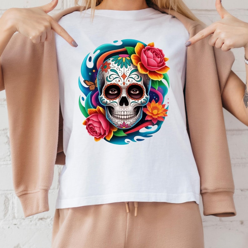 May include: White t-shirt featuring a colorful sugar skull design. The skull is decorated with intricate patterns and surrounded by vibrant flowers and a blue swirl. A butterfly is also included in the design.