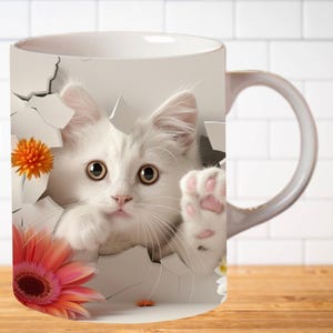 Pu&ograve; includere: Tazza in ceramica bianca con un'immagine 3D di un gattino bianco che spunta da un buco con zampe rosa e fiori. Il gattino ha grandi occhi rotondi e un'espressione sorpresa.