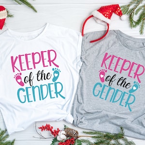 May include: Two white t-shirts with the text "Keeper of the Gender" in pink and blue with a pink and blue footprint graphic.