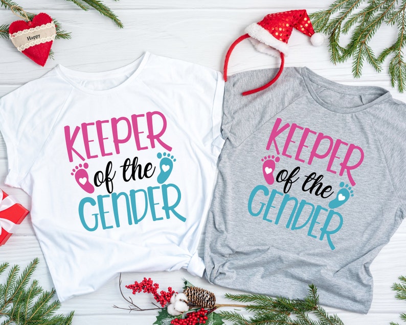 May include: Two white t-shirts with the text "Keeper of the Gender" in pink and blue with a pink and blue footprint graphic.