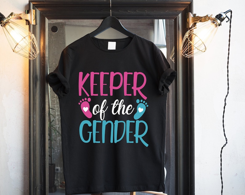 May include: Black t-shirt with the text "KEEPER of the GENDER" in pink and blue lettering.  Two footprints with hearts are above the word "GENDER".