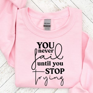 May include: Pink sweatshirt with black text that reads "You never fail until you stop trying."