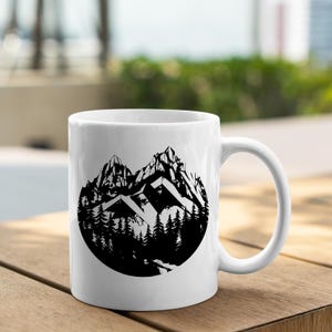 May include: White ceramic mug with a black and white illustration of a mountain range and trees in a circle design.