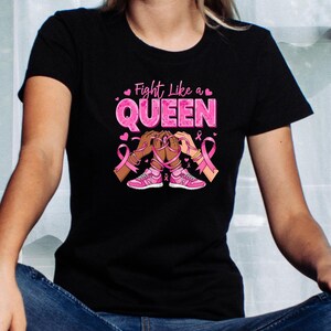 May include: Black t-shirt with a pink graphic that reads "Fight Like a QUEEN." The graphic includes pink ribbons, pink sneakers, and illustrations of hands. The shirt is a crew neck.