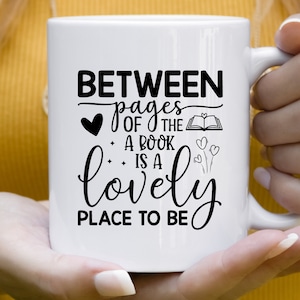 May include: White ceramic mug with black text that reads "Between pages of the book is a lovely place to be". The text is in a cursive font and includes a heart and a book illustration.