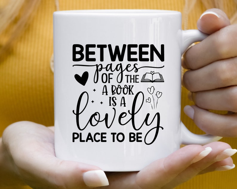 May include: White ceramic mug with black text that reads "Between pages of the book is a lovely place to be". The text is in a cursive font and includes a heart and a book illustration.