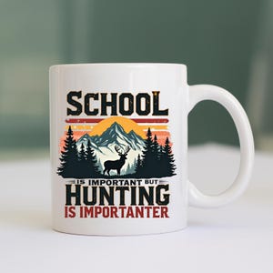 May include: White ceramic mug with a black and orange mountain and forest design. The mug features the text "SCHOOL IS IMPORTANT BUT HUNTING IS IMPORTANTER" in black and orange lettering. A deer silhouette is also included.