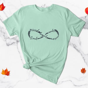 May include: A light green t-shirt with an infinity symbol design. The symbol is made up of the words "Missed beyond words measure" and "Loved".