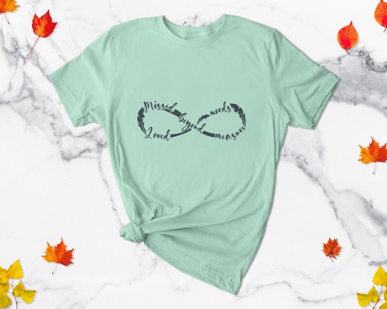 May include: A light green t-shirt with an infinity symbol design. The symbol is made up of the words "Missed beyond words measure" and "Loved".
