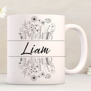 Puede incluir: Taza de cer&aacute;mica blanca con un contorno negro de flores y el nombre "Liam" impreso en la parte delantera.