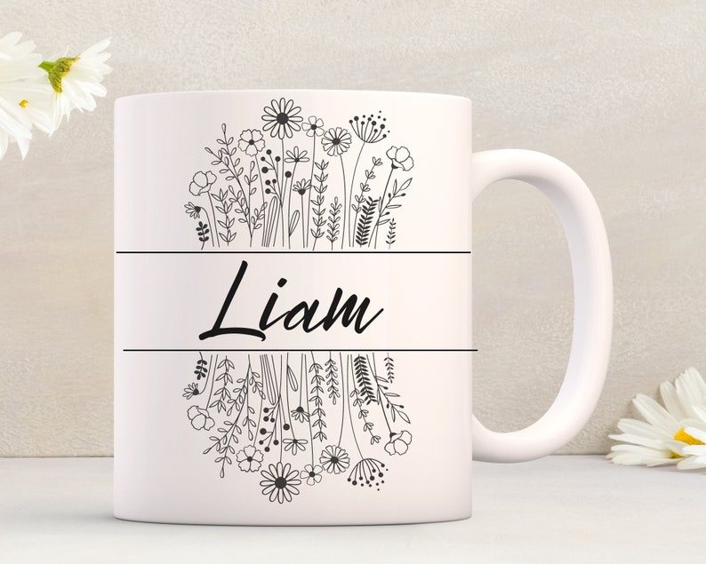 Puede incluir: Taza de cer&aacute;mica blanca con un contorno negro de flores y el nombre "Liam" impreso en la parte delantera.