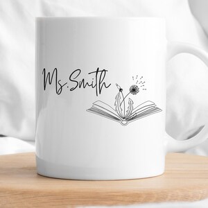 May include: White ceramic mug with a black outline of a book and dandelion with the text "Ms. Smith" on the front.