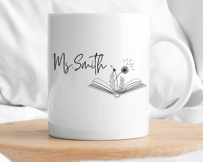 May include: White ceramic mug with a black outline of a book and dandelion with the text "Ms. Smith" on the front.