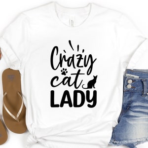 Może przedstawiać: Biała koszulka z czarnym napisem "Crazy cat lady" z odciskiem łapy i czarną sylwetką kota.