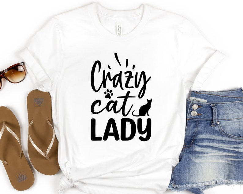 Może przedstawiać: Biała koszulka z czarnym napisem "Crazy cat lady" z odciskiem łapy i czarną sylwetką kota.