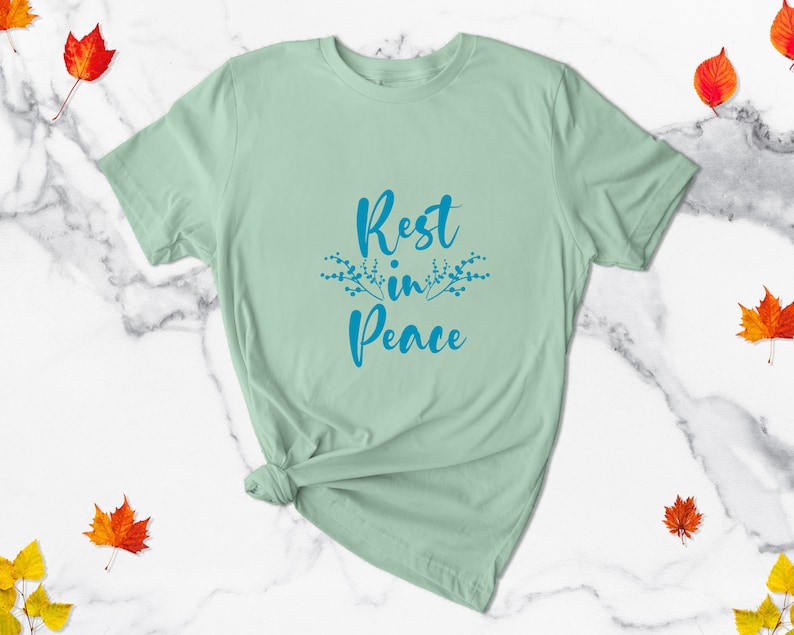May include: A light green t-shirt with the text "Rest in Peace" in blue lettering with a floral design on either side of the text.