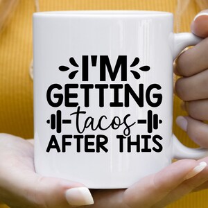 Op de afbeelding: Witte keramische koffiemok met zwarte tekst die "Ik ga na deze training tacos eten" luidt, met een halter afbeelding aan weerszijden van het woord "tacos".