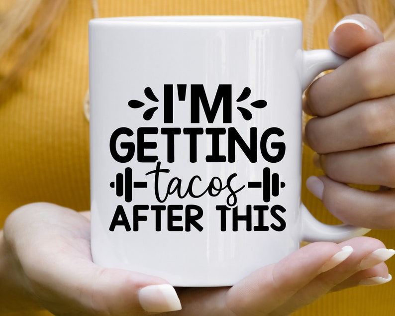 Op de afbeelding: Witte keramische koffiemok met zwarte tekst die "Ik ga na deze training tacos eten" luidt, met een halter afbeelding aan weerszijden van het woord "tacos".
