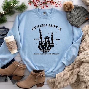 May include: Light blue sweatshirt with a black graphic of a skeleton hand making a rock and roll sign. The graphic includes the text "Generation X", "1965", "1980", and "Raised on hose water & neglect".