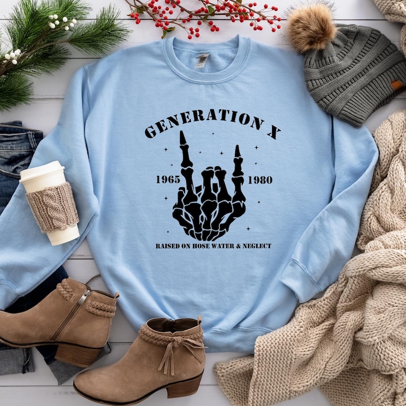 May include: Light blue sweatshirt with a black graphic of a skeleton hand making a rock and roll sign. The graphic includes the text "Generation X", "1965", "1980", and "Raised on hose water & neglect".