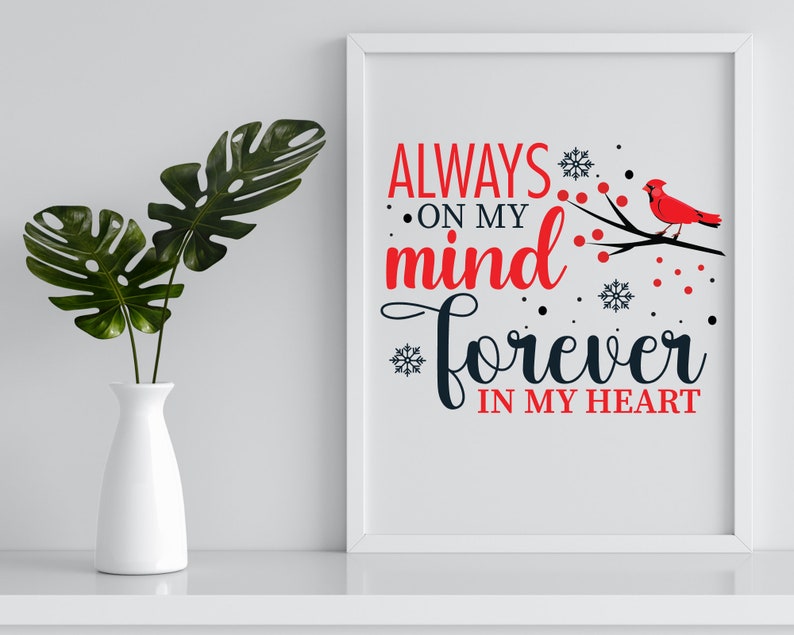 May include: A white framed print with a black and red design. The text reads "Always on my mind forever in my heart". A red cardinal bird is perched on a branch with red berries and snowflakes.