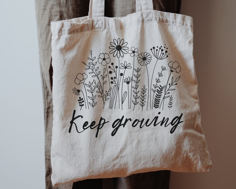 Puede incluir: Una bolsa de tela blanca con dibujos de flores en negro y el texto "Keep growing".