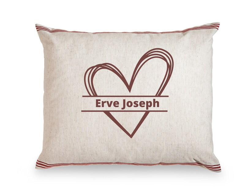 May include: A white pillow with red stripes around the edges. A brown heart with the text "Erve Joseph" inside is printed on the pillow.