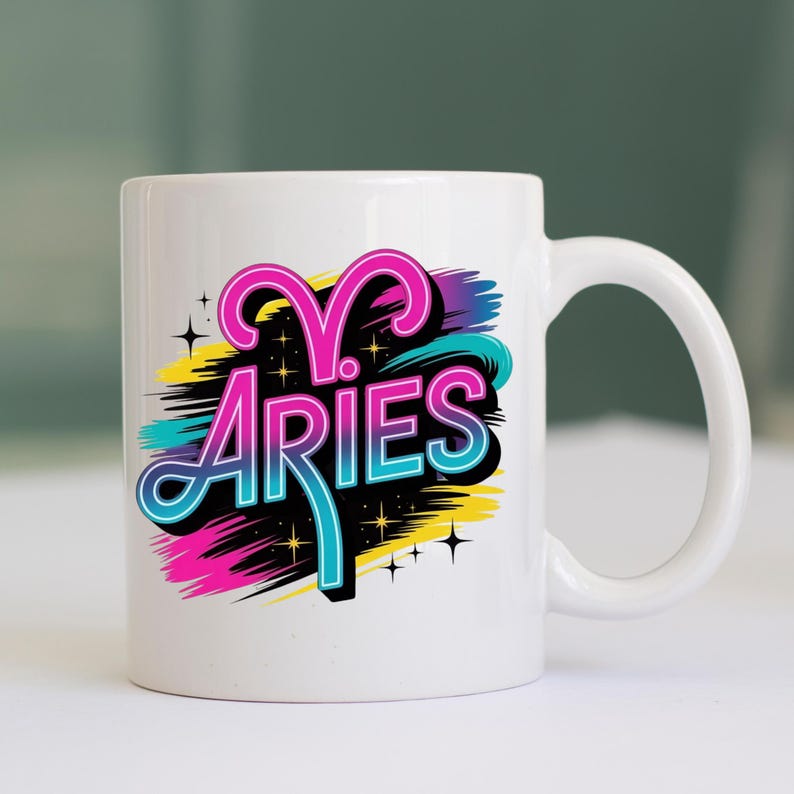 Op de afbeelding: Witte keramische mok met het woord "ARIES" in een kleurrijk, gestileerd ontwerp. Het ontwerp bevat roze, blauwe, gele en zwarte elementen, met steraccenten. De mok heeft een gebogen handvat.