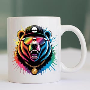 May include: White ceramic mug featuring a colorful illustration of a bear wearing a black cap with a skull, rainbow sunglasses, and a gold chain. The bear has an open mouth and is surrounded by colorful paint splatters.
