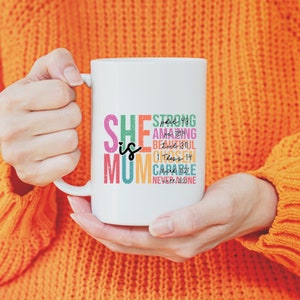 K&ouml;nnte beinhalten: Wei&szlig;e Keramiktasse mit einem bunten Design, auf dem "She is Mum" steht und Bibelverse und inspirierende Worte wie "Strong", "Amazing", "Beautiful", "Chosen", "Capable" und "Never Alone" enthalten sind.