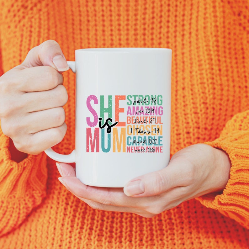 K&ouml;nnte beinhalten: Wei&szlig;e Keramiktasse mit einem bunten Design, auf dem "She is Mum" steht und Bibelverse und inspirierende Worte wie "Strong", "Amazing", "Beautiful", "Chosen", "Capable" und "Never Alone" enthalten sind.